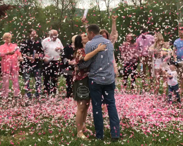 A couple kissing, while their friends and family fire off pink confetti cannons all around them.