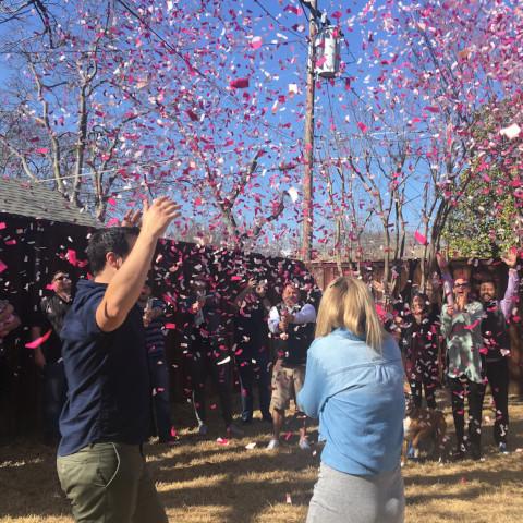 Family and friends shooting pink confetti outside while surrounding couple