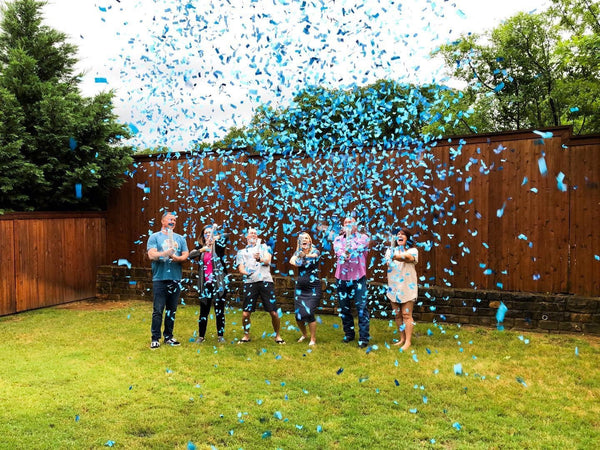 Family posing outside with blue confetti, announcing the couple having a baby boy.