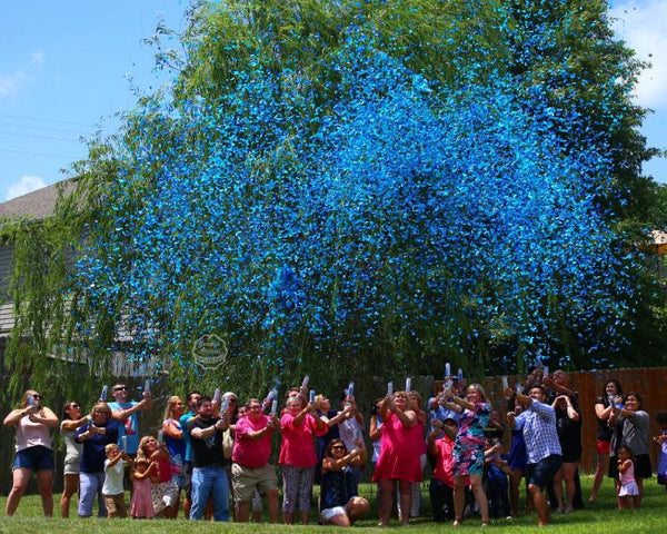 Couple posing with family and friends outside while shooting blue confetti into the air.