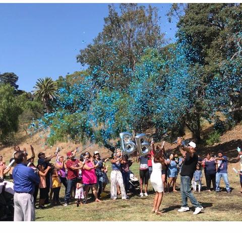 Couple posing with family and friends outside while shooting blue confetti up in the air