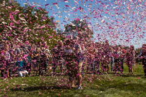 Couple celebrating having a girl with family and friends by shooting pink confetti.