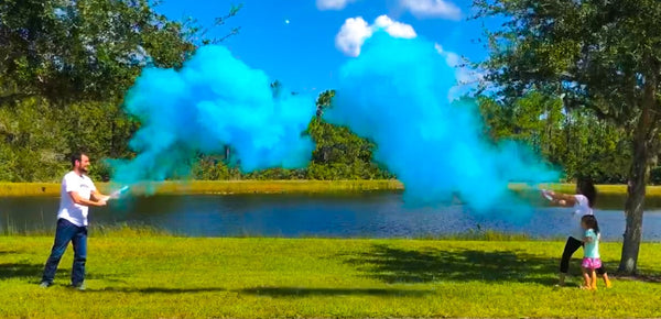 Couple posing by a lake with blue smoke announcing them having a baby boy.