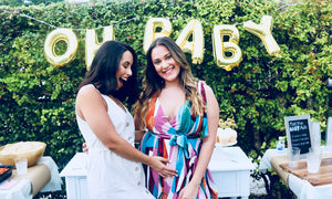 Pregnant woman and friend posing for a picture in front of a "oh baby" sign outside.