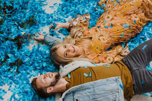 Couple laying down in blue confetti celebrating having a baby boy.