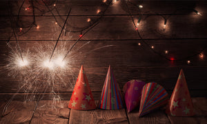 Sparklers and party hats staged on a wood table for a picture.