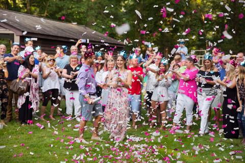 Family and friends surrounding a couple outside, while shooting pink confetti cannons.