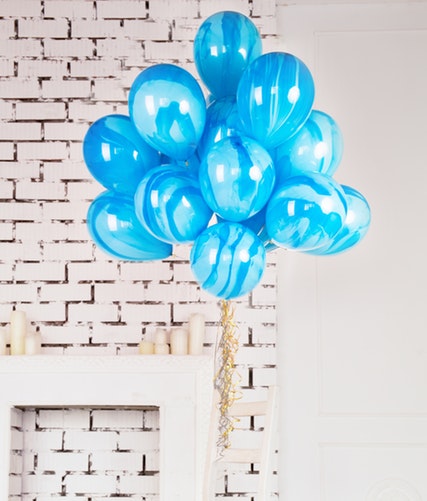 blue balloons tied to a table with a white brick wall as a background.