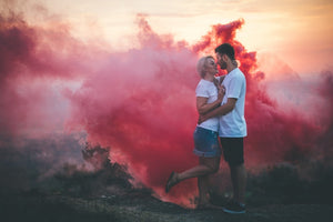 Couple posing outside with pink smoke in the background.