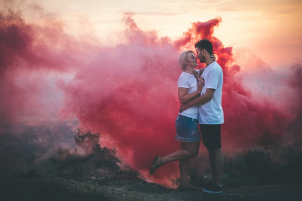 Couple posing outside with pink smoke in the background.