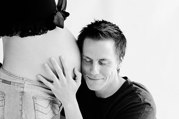 Man posing with his ear up against a woman's pregnant belly.