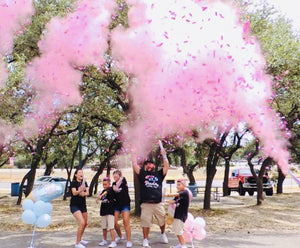 Family posed with pink smoke and confetti in the air outside.