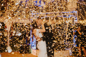 Couple posing at a wedding while gold confetti falls all around them.